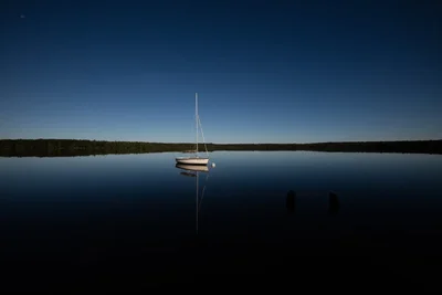 sailboat anchored on calm lake at dusk