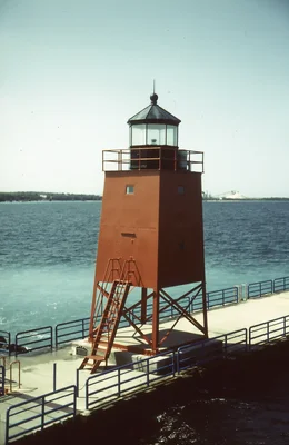 rust colored lighthouse on concrete pier over water